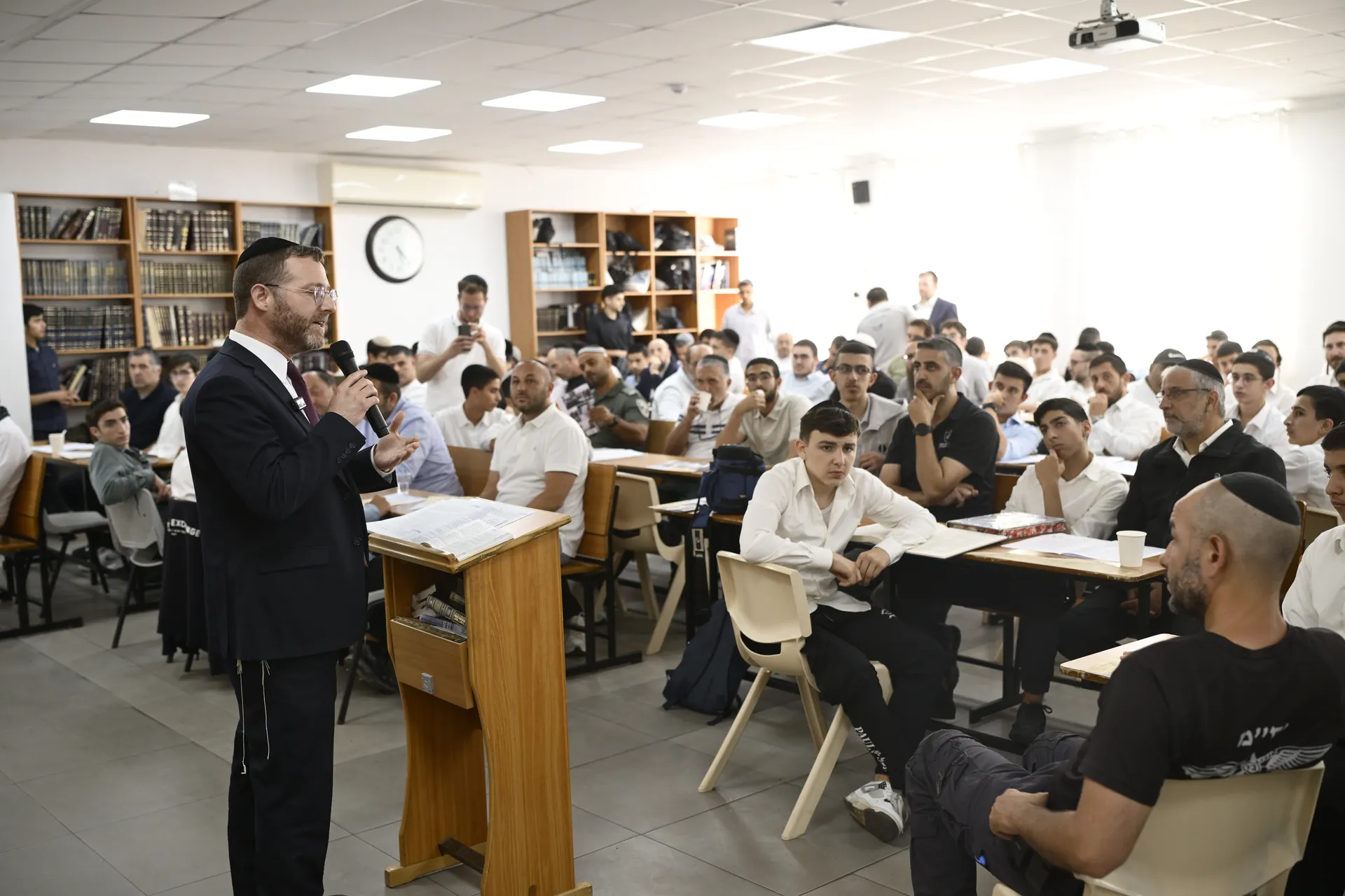 רב מדבר מול אולם מלא באבות ובנים בבית המדרש של זיו אור נתניה