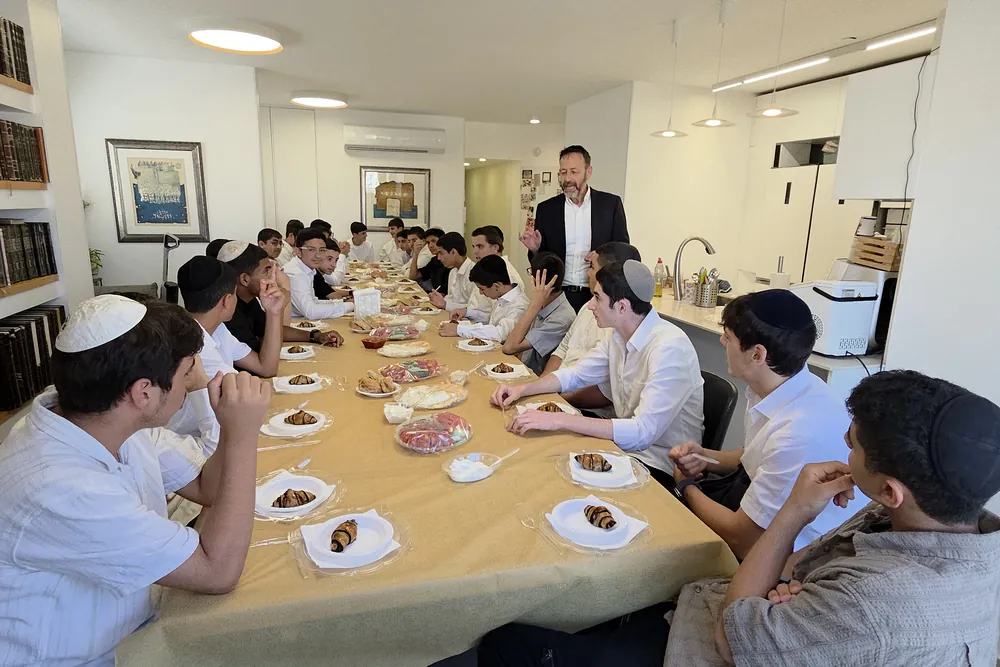 מורה מסביר לתלמידים ליד ספריית ספרים - בוקר ערכי לשיעור א׳ בראש חודש תמוז