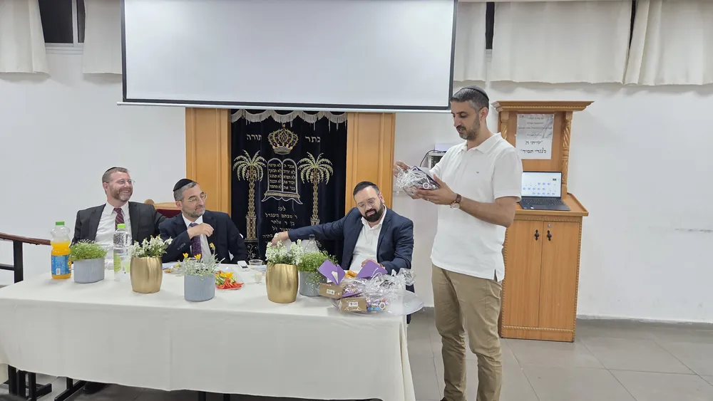 איש בחולצה לבנה מציג מתנה ליד שולחן הכבוד - מסיבת סיום לשיעור ד׳