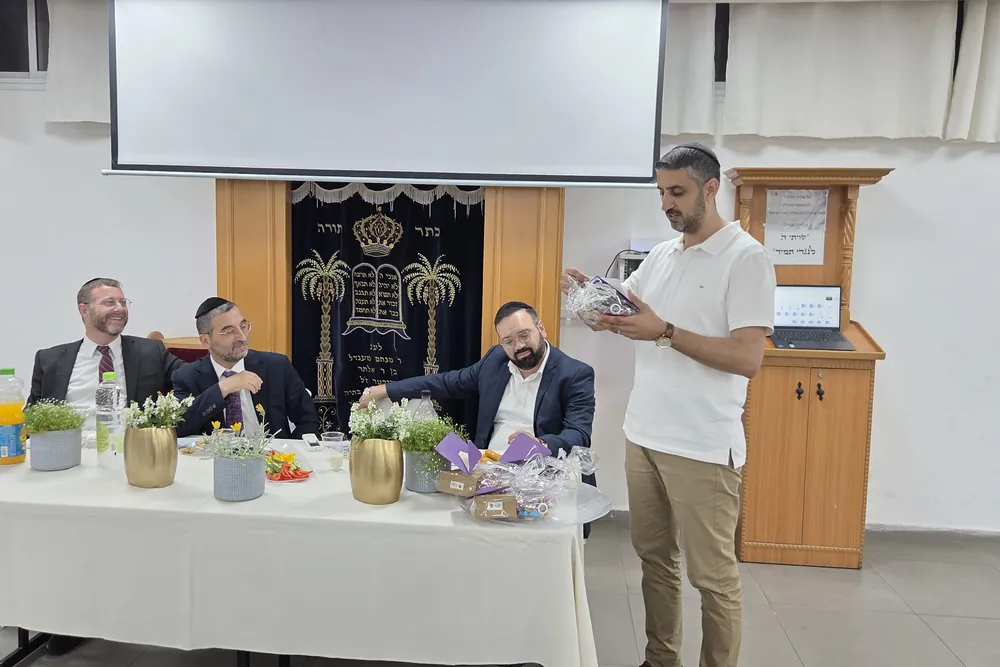 איש בחולצה לבנה מציג מתנה ליד שולחן הכבוד - מסיבת סיום לשיעור ד׳