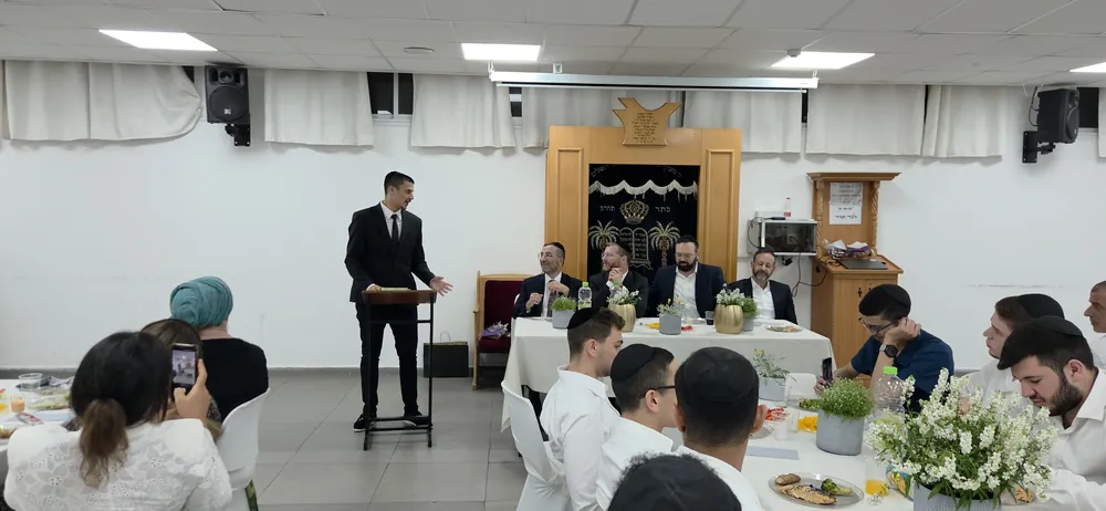 תלמיד בחליפה נואם ליד שולחן הכבוד - מסיבת סיום לשיעור ד׳