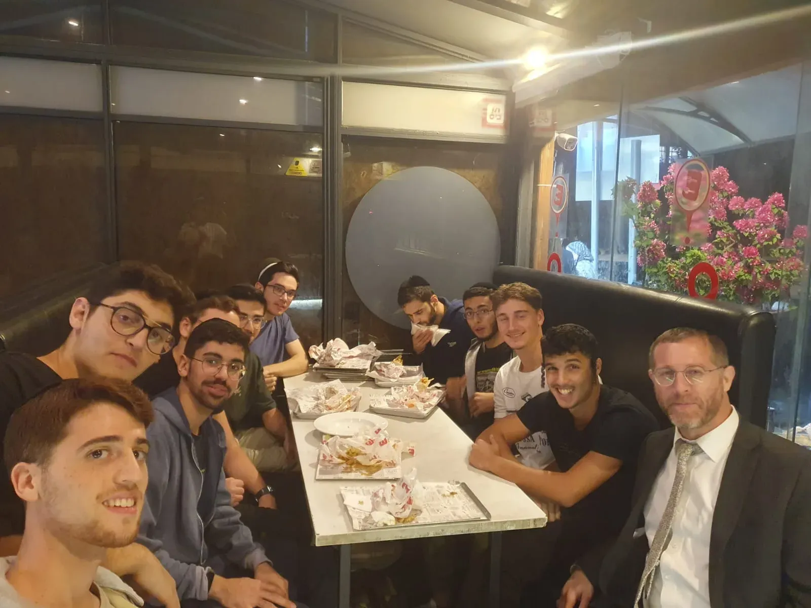 קבוצת תלמידים וחבר צוות יושבים יחד בארוחה במסעדה בערב