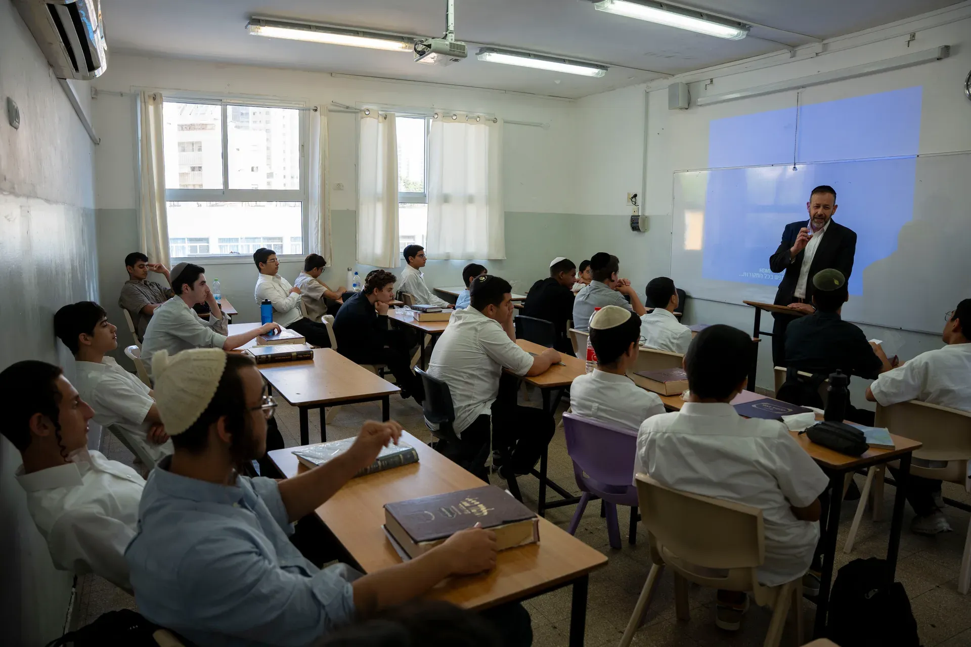מורה מלמד שיעור מול כיתה, מסך הקרנה כחול ברקע