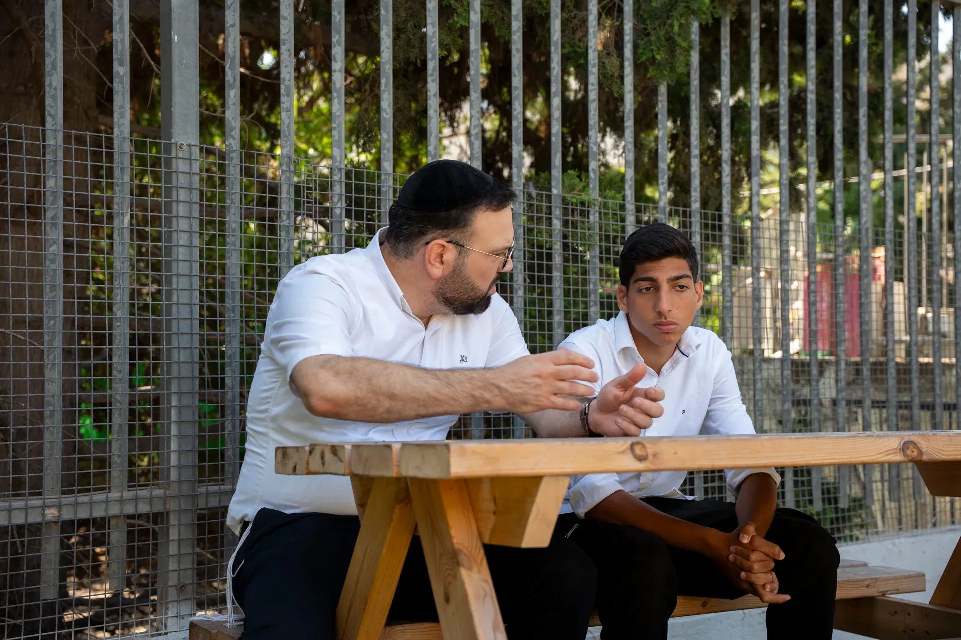 רב בשיחה אישית עם תלמיד, יושבים יחד ליד שולחן בחוץ