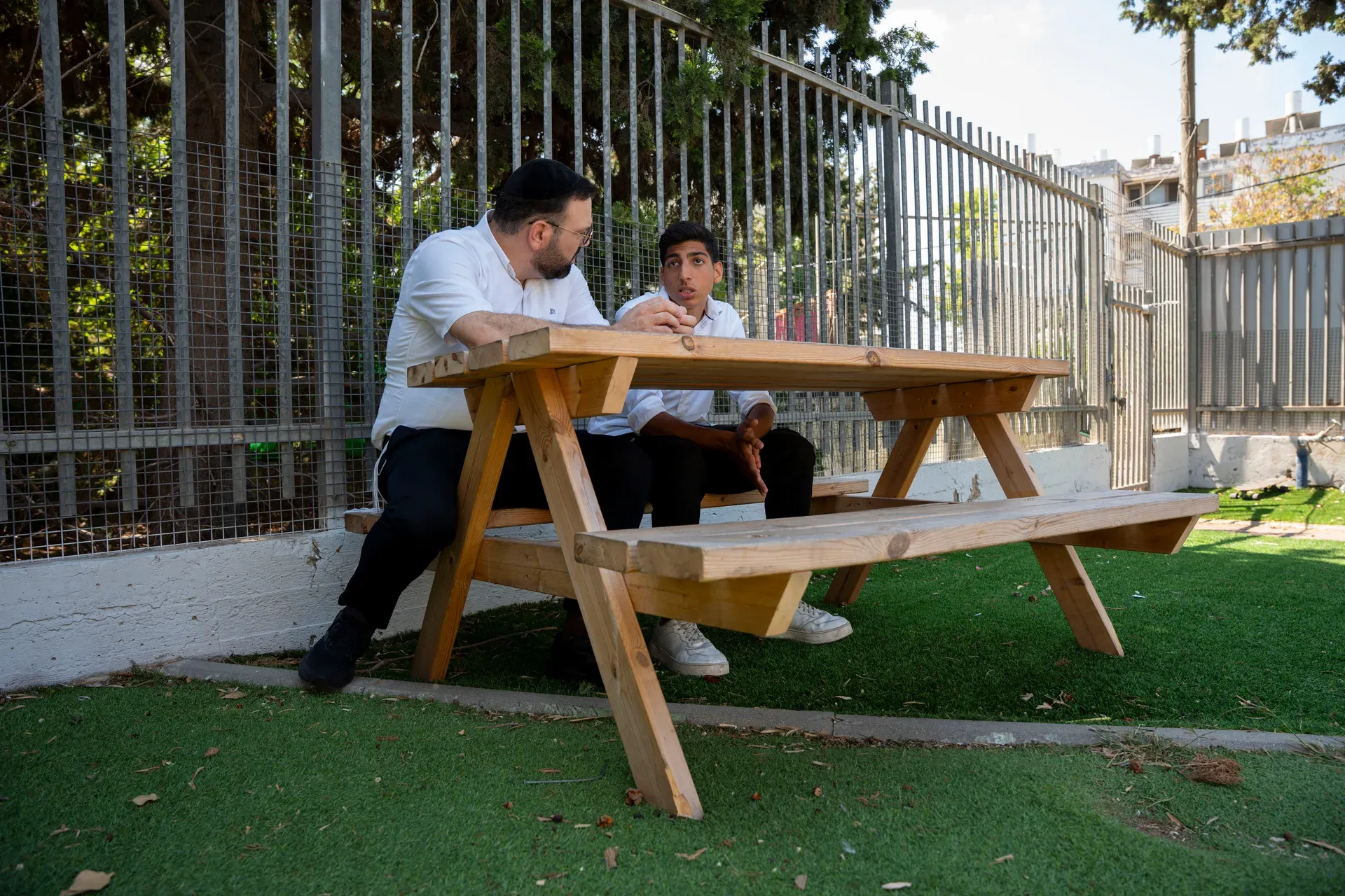 רב בשיחה עם תלמיד, יושבים יחד ליד שולחן בחוץ